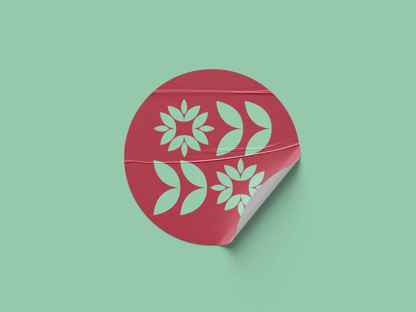 Round red KERA sticker with mint flower and leaf ornaments, one edge peeling up